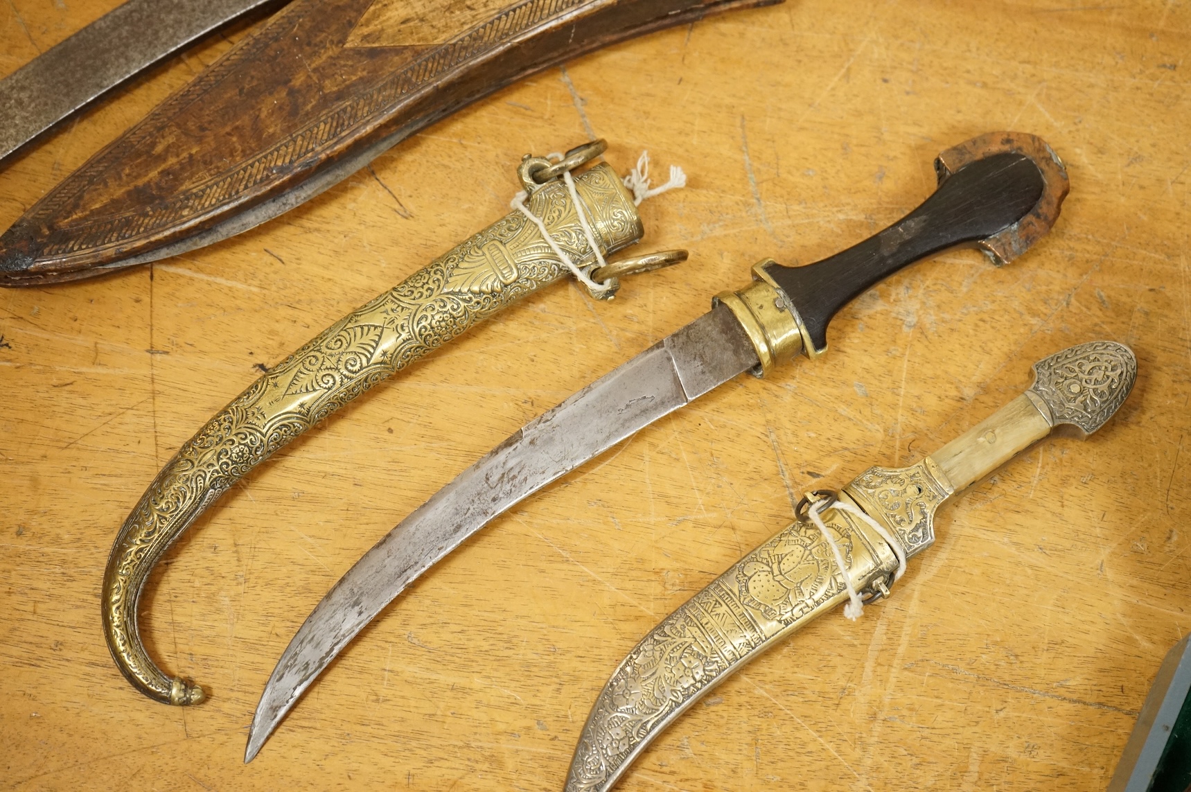 An Indian sword tulwar, the iron hilt with traces of chiselled and inlaid decoration, together with a kukri in its wooden scabbard, a Syrian jambya and a Moroccan jambiya (4)